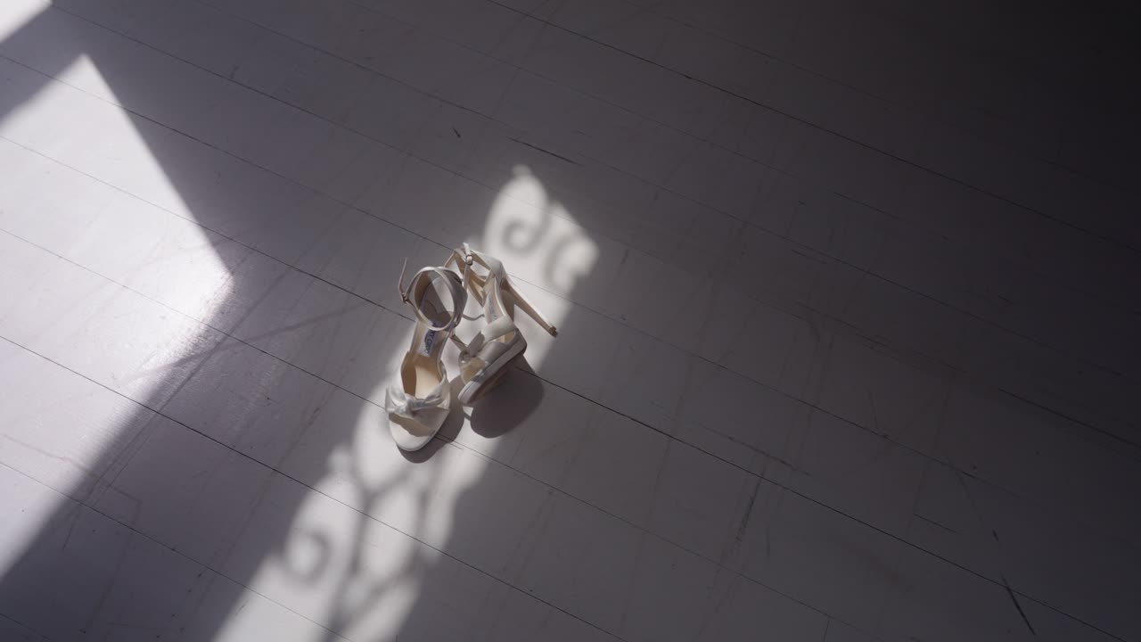A pair of bridal shoes placed on the floor with soft sunlight streaming through a window, casting elegant shadows and creating a warm, intimate wedding atmosphere