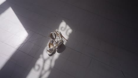 a pair of bridal shoes placed on the floor with soft sunlight streaming through a window, casting elegant shadows and creating a warm, intimate wedding atmosphere