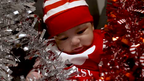 Adorable-Bebé-De-2-Meses-Vestido-Con-Traje-Rojo-De-Navidad-Y-Sombrero-Y-Siendo-Juguetón-Con-Oropel-Rojo-Y-Plateado-Lo-Rodeó-En-El-Sofá