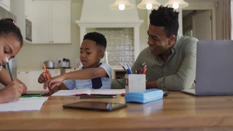 Padre-Afroamericano,-Hija-E-Hijo-Sentados-En-La-Mesa-De-La-Cocina-Haciendo-La-Tarea