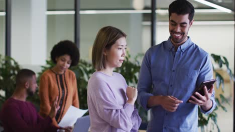 Diverse-business-people-talking-using-a-digital-tablet-in-modern-office