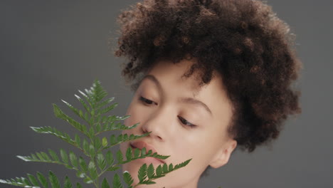 retrato de cerca hermosa mujer de raza mixta tocando la cara con hojas de helecho acariciando piel suave y saludable disfrutando de la belleza natural juguetona sobre un fondo gris concepto de cuidado de la piel