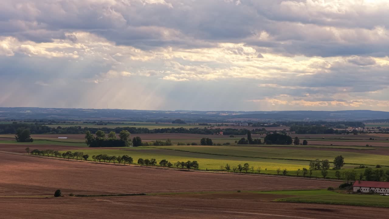 Sky with clouds with rays of sun shining through falling on the landscape of fields and meadows. Sunny day in the Czech Republic
