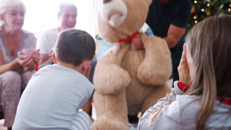 children playing with giant teddy bear as multi-generation family open gifts on christmas day