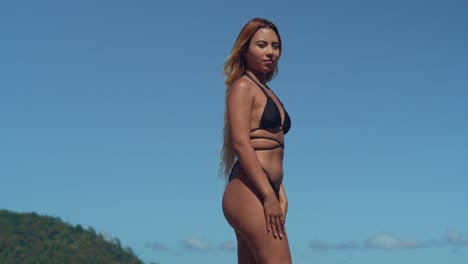 una joven hispana vestida de bikini se bacia en la serenidad de una playa tropical del caribe con arena blanca prístina y cielos azules en el fondo