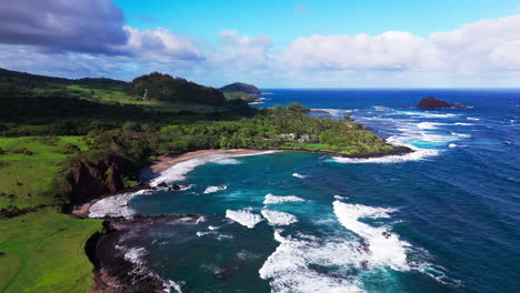 cinematic-drone-pull-away-shot-of-large-and-big-waves-crashing-into-the-rocks-during-a-sunny-and-hot-day-by-the-beach-in-hawaii