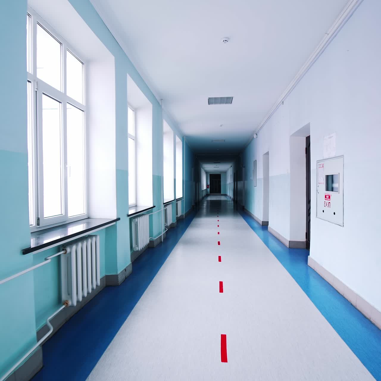 Motion along the corridor inside empty college. Blue long hallway with big windows in modern university