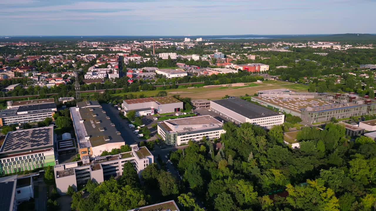 Modern film studios with offices and sound stages surrounded by trees in Berlin Adlershof, Germany. Unique aerial view flight wide orbit overview drone
