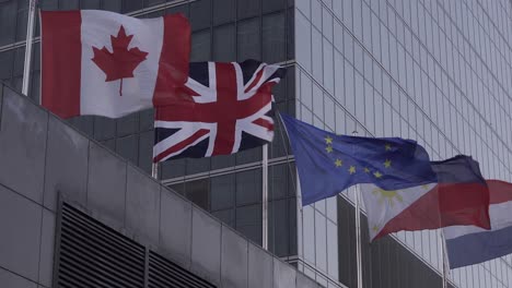 Flagge-Kanadas,-Des-Vereinigten-Königreichs,-Der-Europäischen-Union,-Der-Niederlande-Und-Der-Philippinen-An-Einem-Windigen,-Stürmischen-Tag-Vor-Dem-Geschäftszentrum