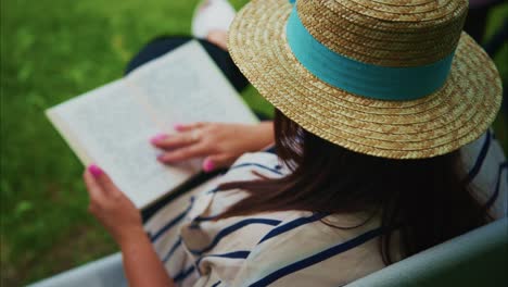 woman wearing straw hat reading a book outdoors in a serene green environment with soft sunlight