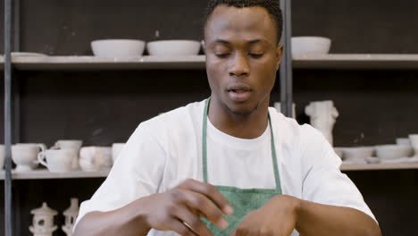 young man packaging handicraft ceramics with paper in the pottery shop while his female colleague working on laptop computer