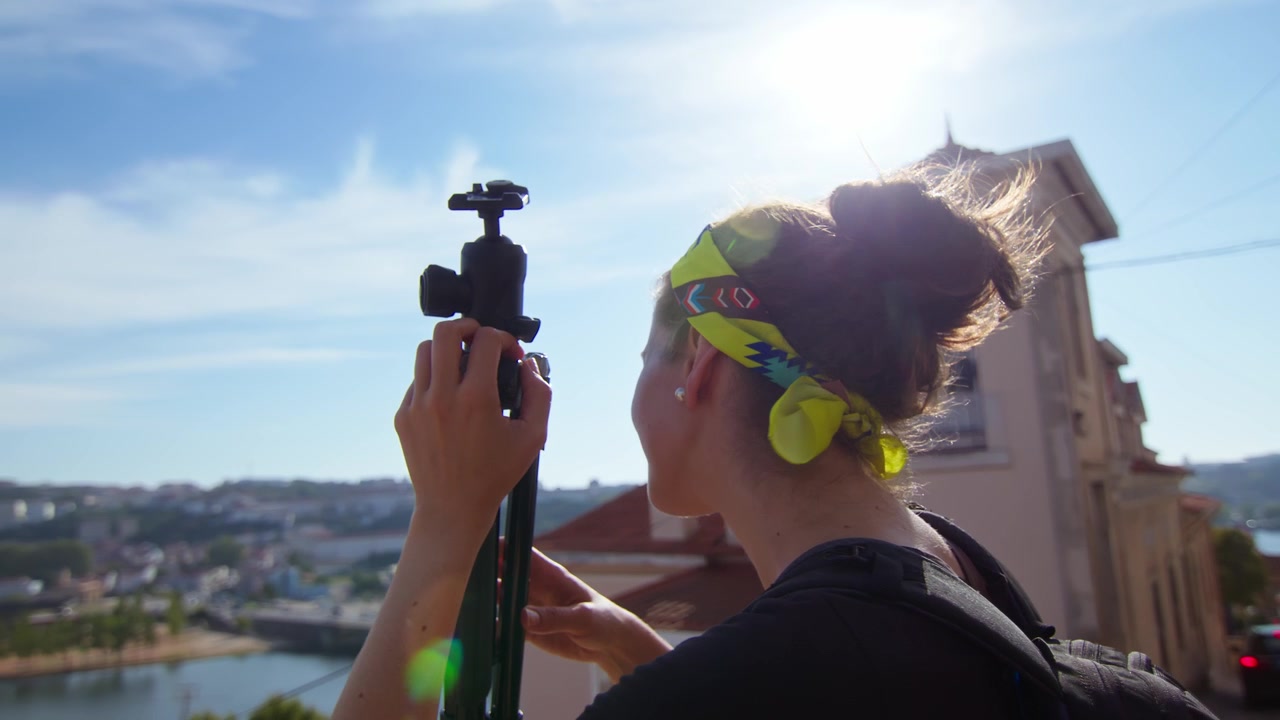 Ragazza con una fascia gialla per capelli, che tiene un treppiede e ammira la vista panoramica a Coimbra, Portogallo.