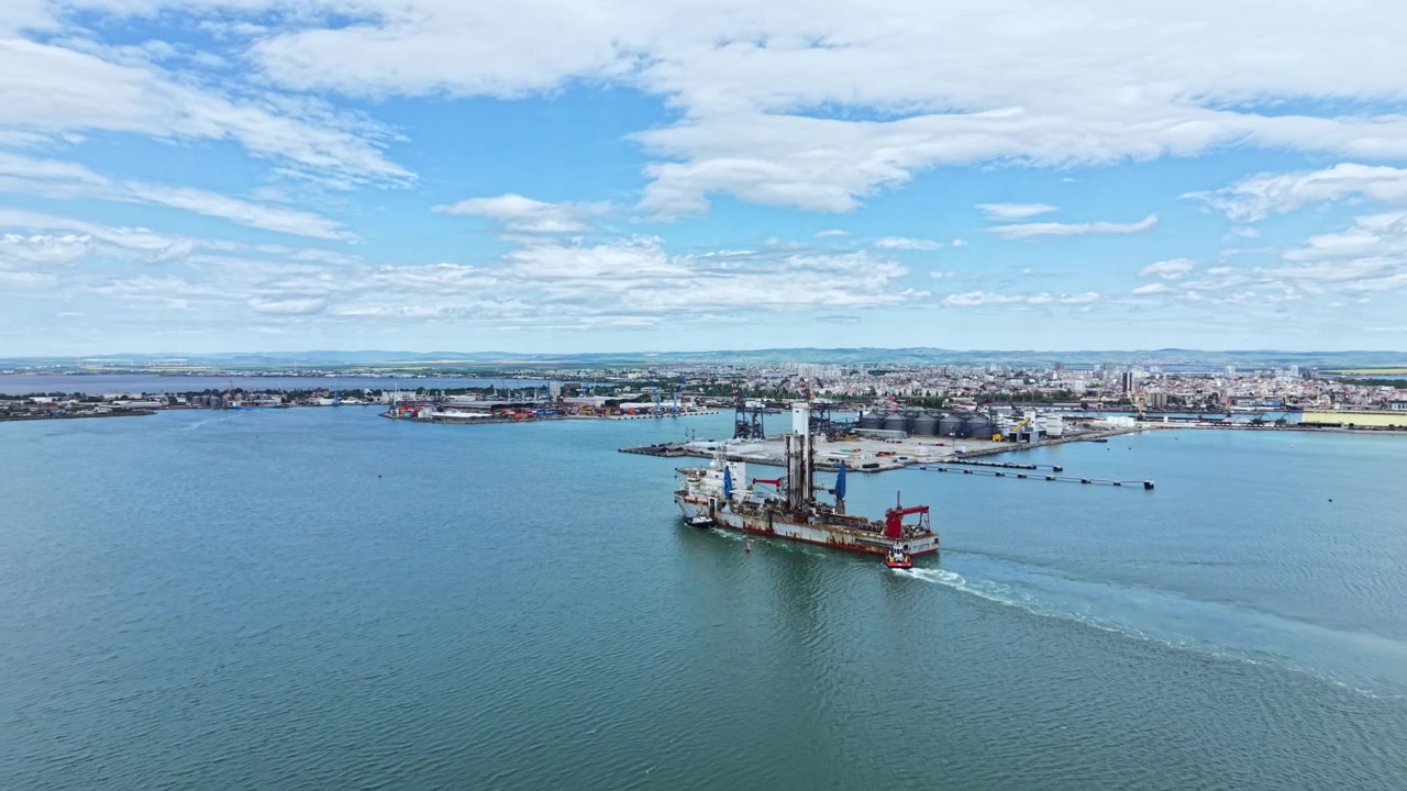 Industrial dredging vessel operates in harbor waters near city under blue sky with scattered clouds