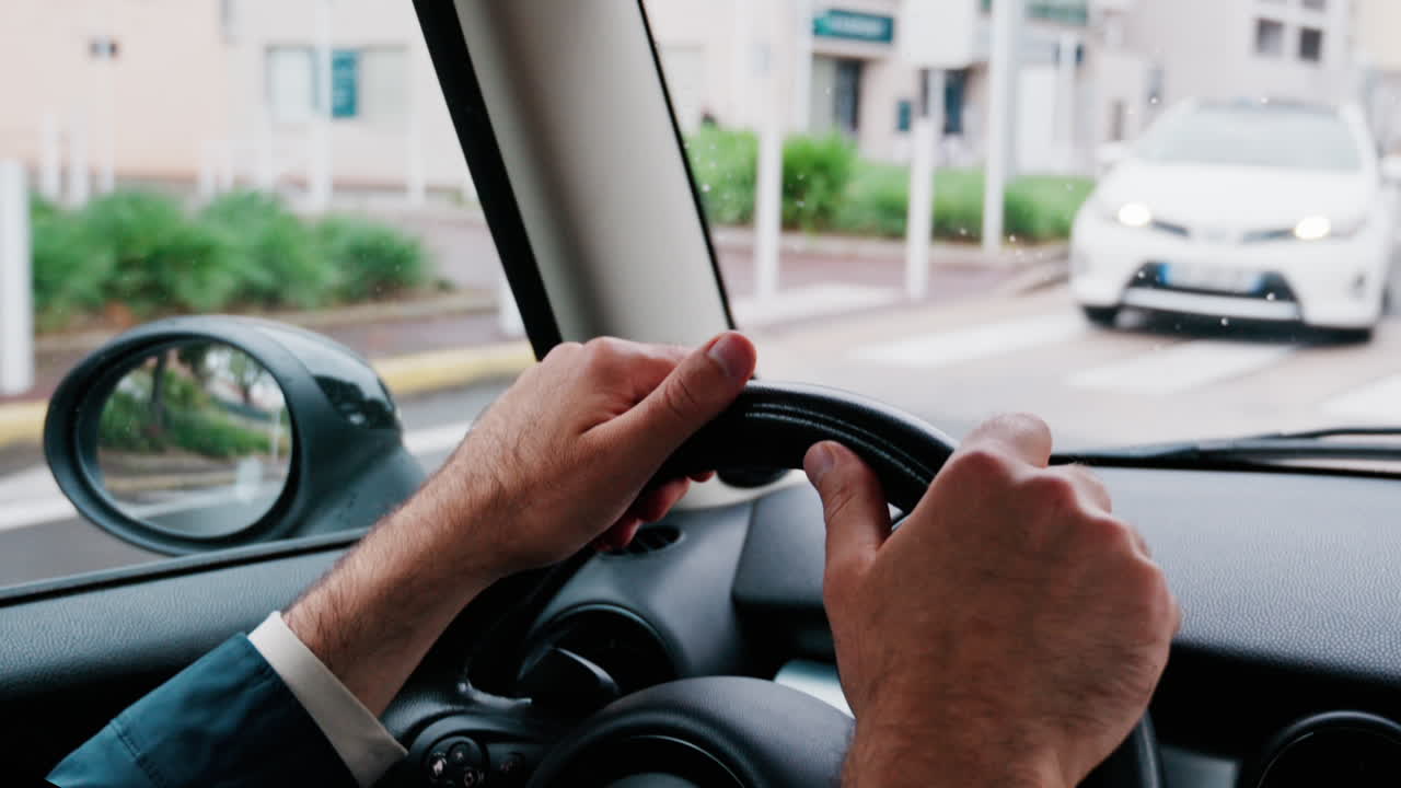 Close up of a man's hands on a steering wheel, driving a car on the road