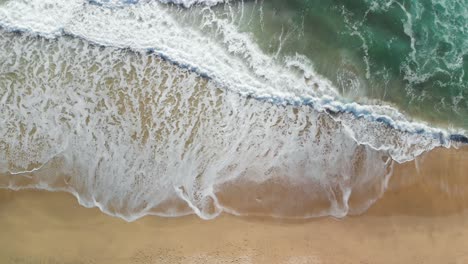 Top-down-aerial-shot-of-the-blue-ocean-waves-crashing-on-the-California-shore-near-Montara