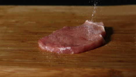 la chuleta de cerdo está siendo sazonada en una mesa de madera.