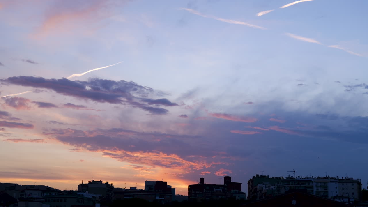 A horizontal panning shot of a vibrant sunset over the city of Mataró, Spain. Colorful clouds, mountain silhouettes, and urban rooftops create a peaceful scenic view.