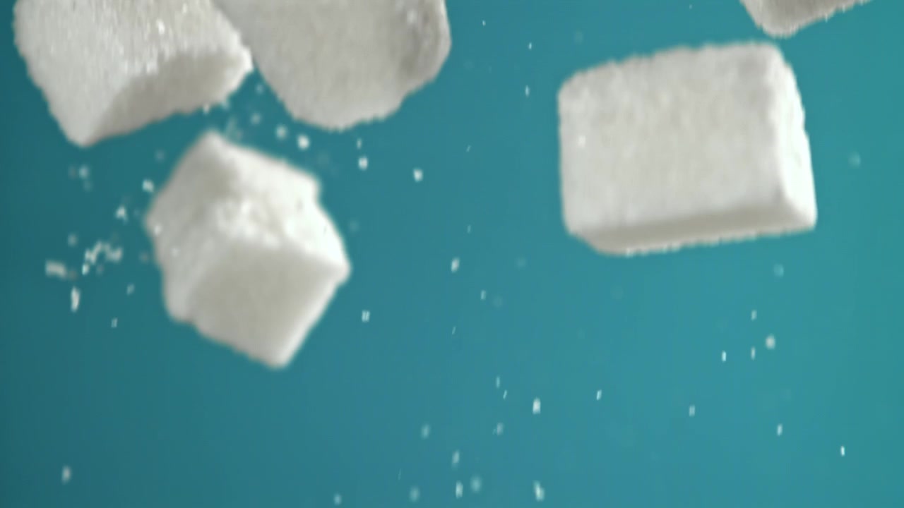 Cubetti di zucchero bianco che cadono al rallentatore su uno sfondo verde acqua