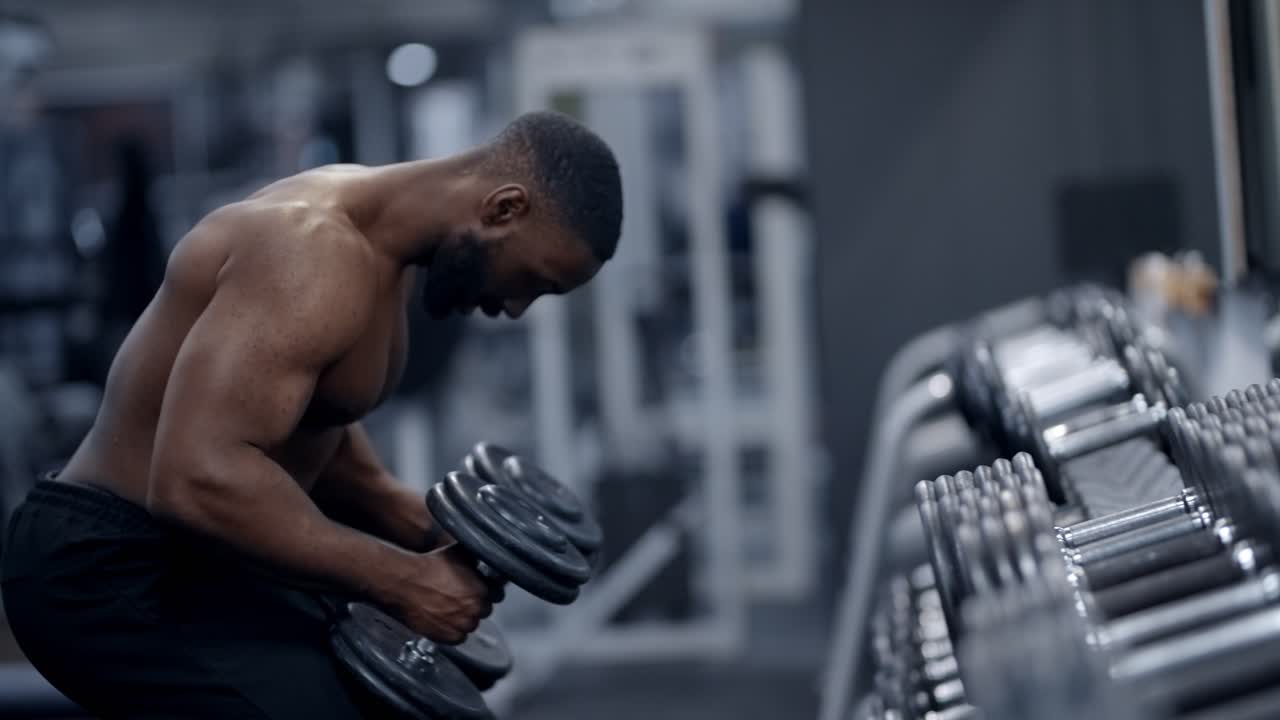 Athletic African American man picking up dumbbells