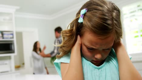chica cubriendo sus orejas mientras los padres discuten en el fondo