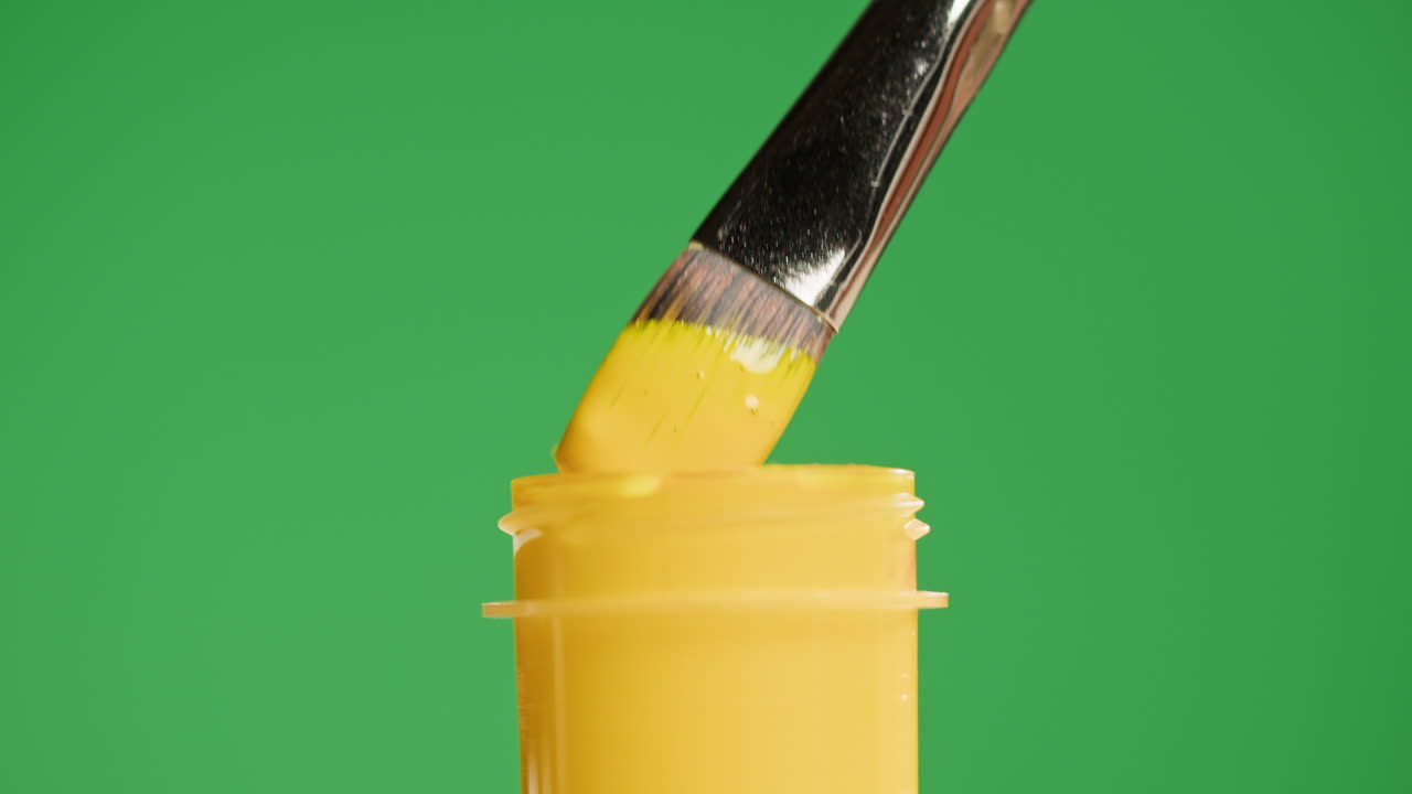 Pennello che si immerge nel barattolo di pittura gialla su green screen