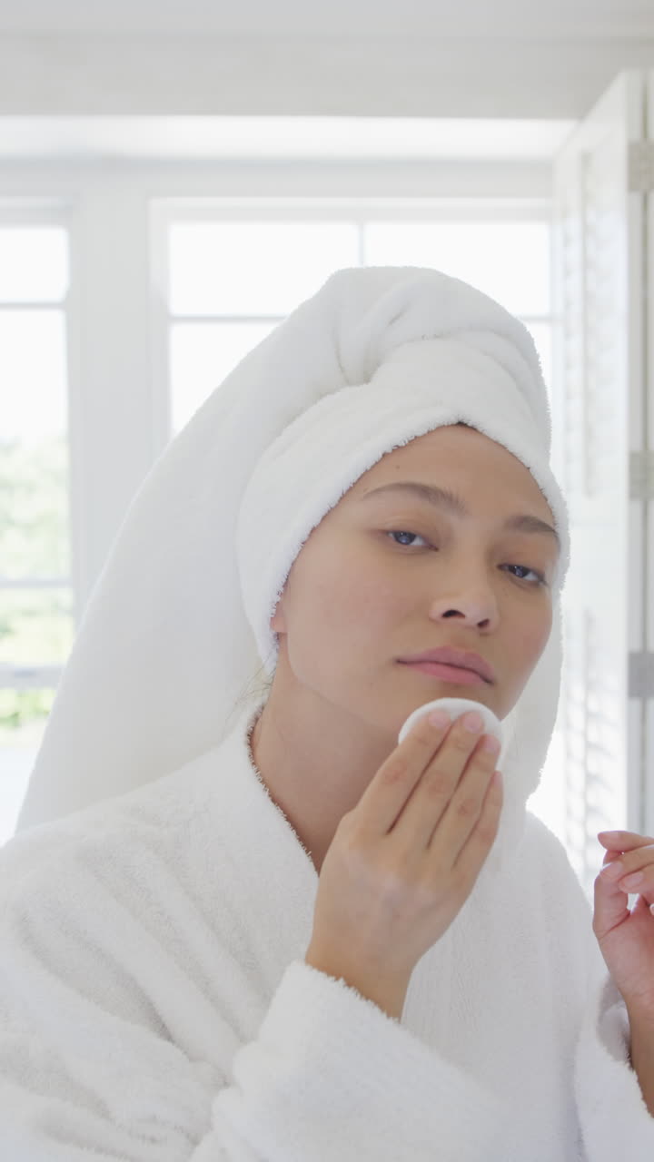 Vertical video of happy asian woman cleansing skin in bathroom, in slow motion