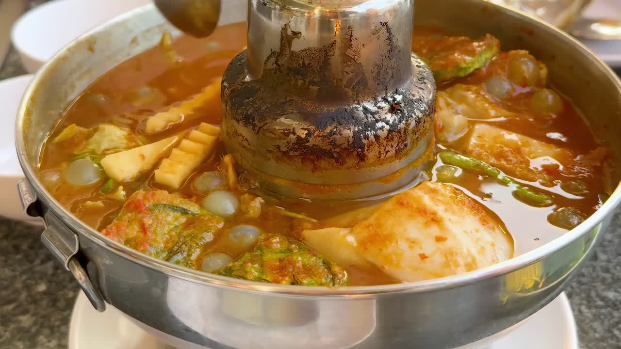 A close-up view of serving hot pot soup filled with vegetables and tofu into a bowl.