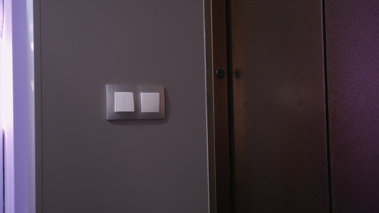 primer plano de una mujer con el cabello atado hacia atrás usando un traje marrón mientras alcanza el interruptor de luz en un interior moderno débilmente iluminado, un brillo suave destaca su silueta mientras se aleja del interruptor