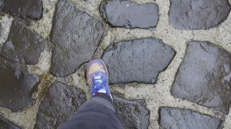 Ripresa in soggettiva di piedi femminili che camminano su una strada asfaltata e lastricata in pietra