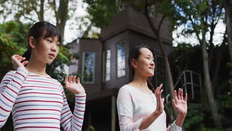 happy asian mother exercising in garden with daughter, practicing tai chi together