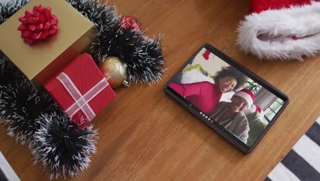 Smiling-african-american-mother-and-daughter-with-santa-hats-on-christmas-video-call-on-tablet