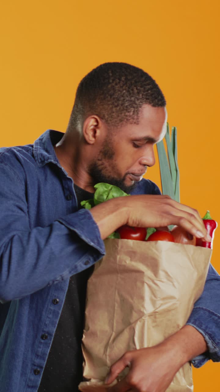 Joven afroamericano oliendo verduras frescas en una bolsa de la compra