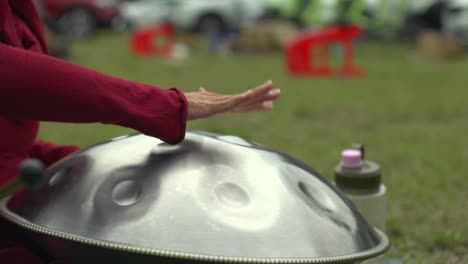 hands and fingers used to tap percussive hand pan instrument, filmed outdoors as medium shot in slow motion