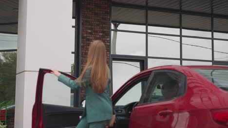 elegant woman gets out of red car looking at modern building