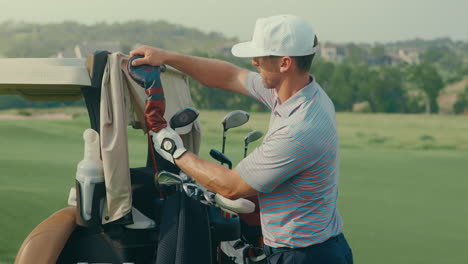 a male golfer pulls the head cover off his three wood from the bag on the back of the golf cart positioned in the middle of the fairway, preparing for his next shot in a natural outdoor course setting