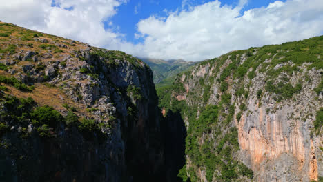 Aerial-drone-forward-moving-shot-of-dried-riverbed-with-steep-cliffs-on-both-sides-alongside-Gjipe-beach-in-Albania-on-a-sunny-day