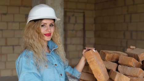 beautiful woman with makeup and manicure holding a brick at the construction site. woman in a helmet and working jeans