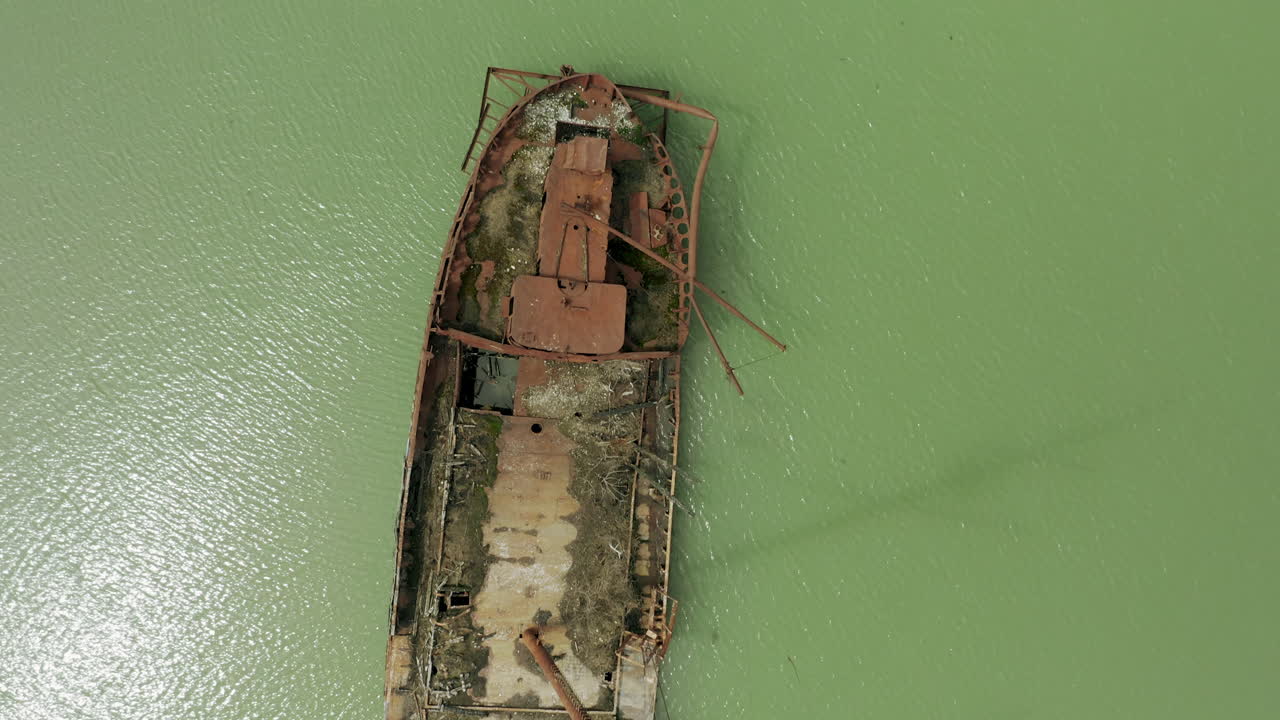 Rusty red shipwreck stuck in shallow green water