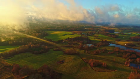 sunset over a lush valley with a river, dramatic clouds casting shadows on the landscape, aerial view