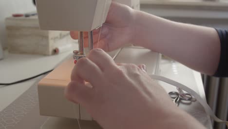 a seamstress threads a needle and stitches a band on a mask being made in response to the coronavirus pandemic