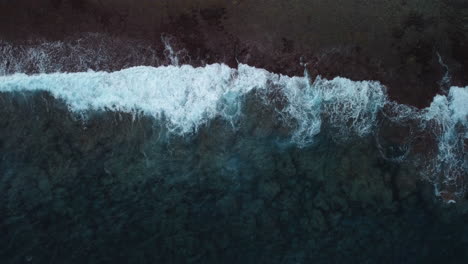 Aerial:-top-down-shot-of-stormy-waves-crashing-on-coastline,-slow-motion