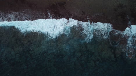 aerial: top down shot of stormy waves crashing on coastline, slow motion