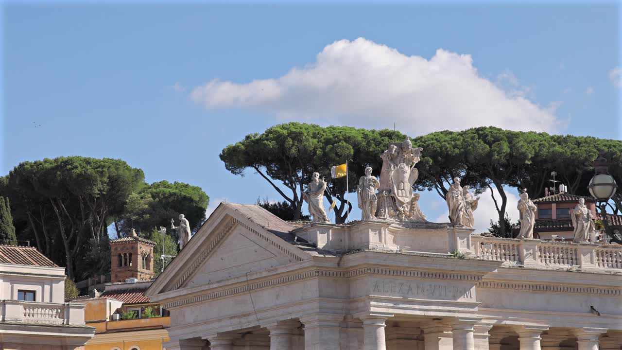 Vatican flag and rooftop statues with pine trees and bright blue sky in the background.