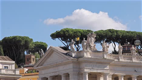 vatican flag and rooftop statues with pine trees and bright blue sky in the background.
