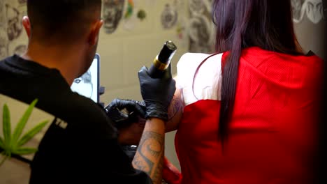 handheld shot reveals a tattoo artist working at the studio tattooing a dog on a woman's arm