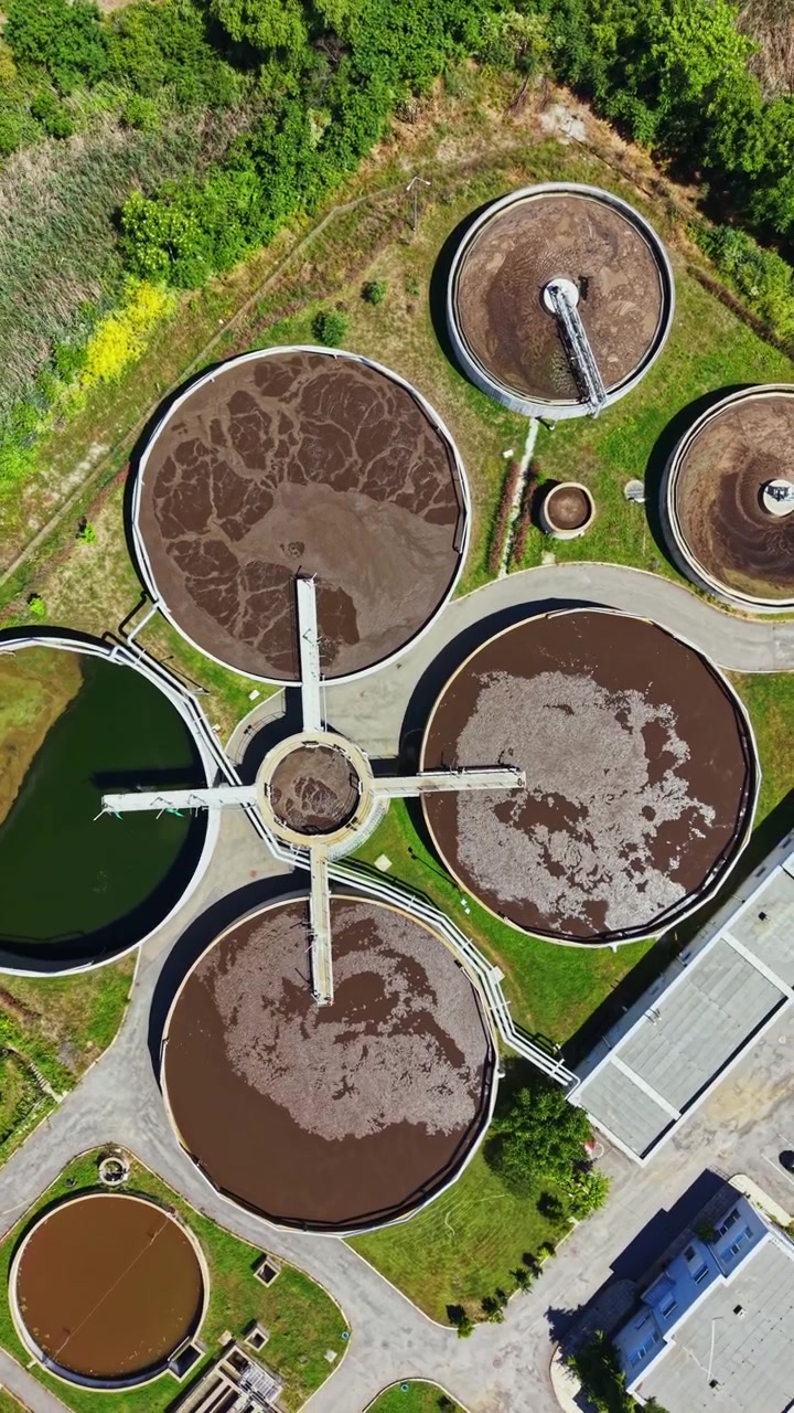 Cuatro grandes tanques de tratamiento vistos desde arriba en una planta de tratamiento de agua durante un día soleado por la tarde.