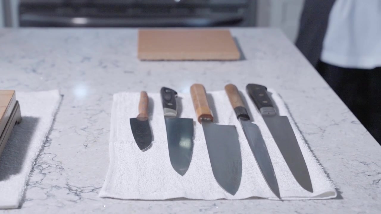 Toma circular que muestra una colección de cuchillos de cocina afilados en la cocina de un chef, destacando herramientas esenciales para la precisión culinaria y la preparación de alimentos. Ideal para contenido culinario y de cocina