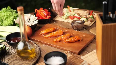 man sprinkles salt on chicken skewers surrounded by grilled vegetables