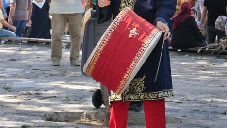 a man in traditional turkish clothing plays a drum in the street