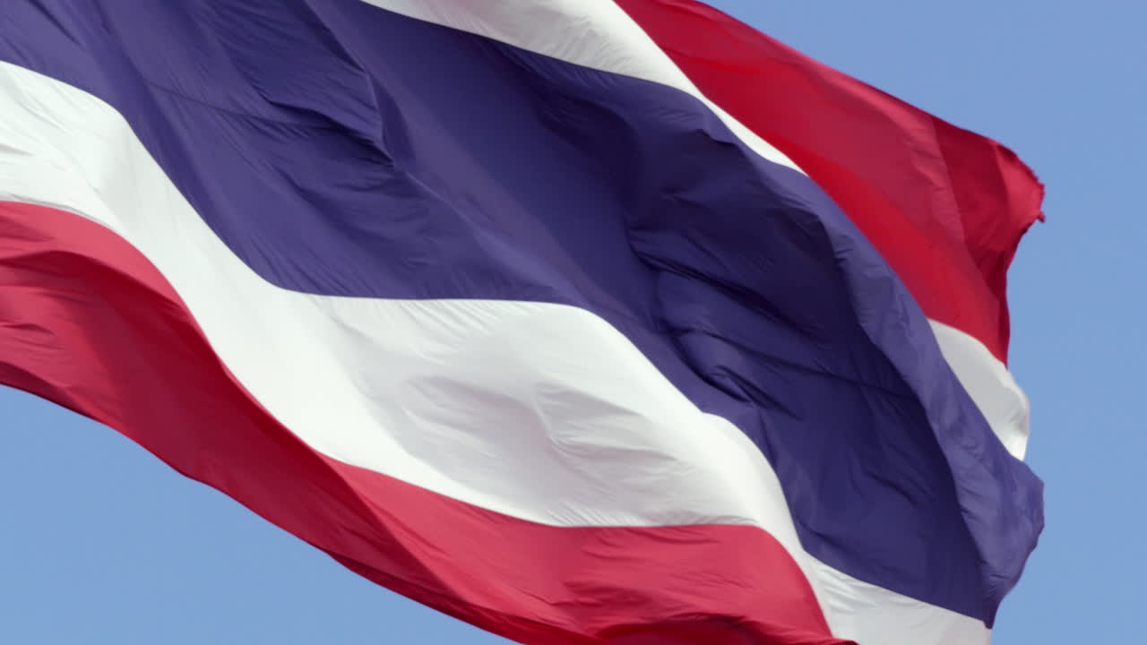 A grand Thai national flag waving in the wind in slow motion with the sky as its backdrop. This peaceful scene represents Thailand's unity, freedom, and the nation's symbolic strength.